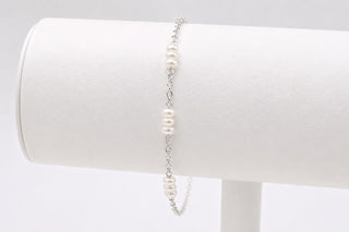 Pearl bracelet on a white cylindrical stand with a plain background