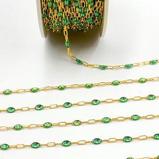 Gold chain with green beads spilling out of a container on a white background